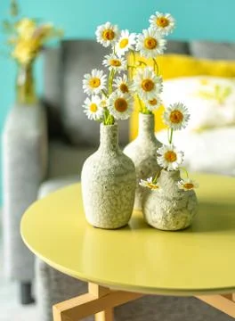 Ceramic vases with daisies on a table in front of a sofa Foto stock