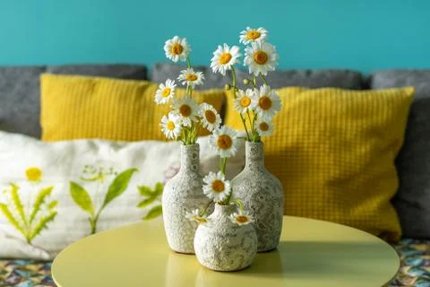 Ceramic vases with daisies on a table in front of a sofa Stock Photos