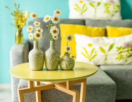 Ceramic vases with daisies on a table in front of a sofa Stock Photos