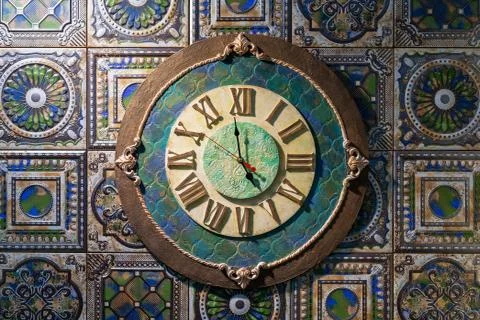 Ceramic wall clock with roman dial against the background of fireplace tiles. Stock Photos