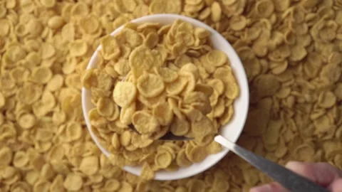 Cereal background with white bowl of cornflakes and spoon in hand scooping and Stock Footage 242293418