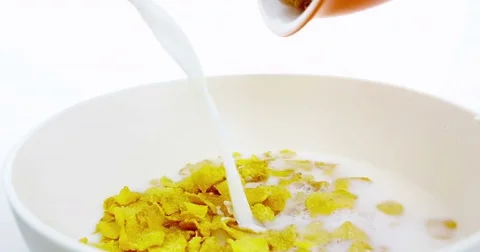 Cereal corn flakes falling down in a bowl pouring with milk on white backgroud Stock-Footage 79995221