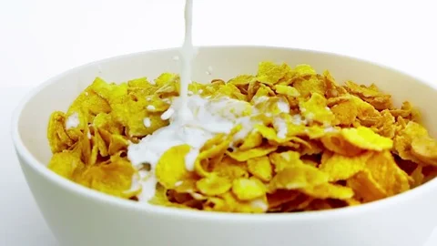 Cereal corn flakes falling down in a bowl pouring with milk on white background Stock Footage 81087915