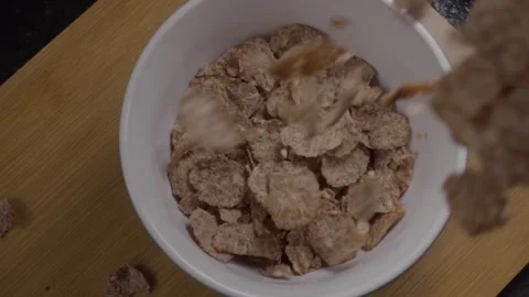 Cereal Flakes Being Poured into White Bowl on Wooden Table Stock Footage 343708204