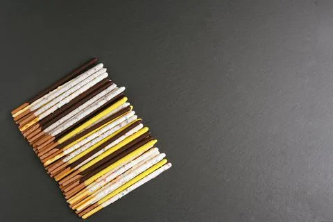 Cereal straw in multi-colored glaze lies in a row on a dark surface Stock Photos