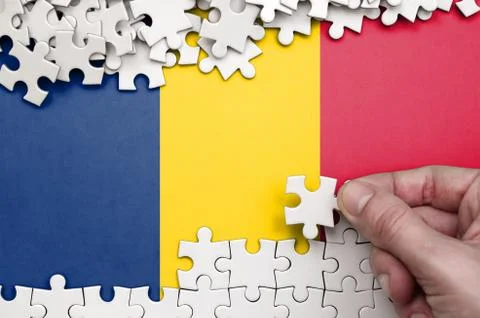 Chad flag  is depicted on a table on which the human hand folds a puzzle of w 写真素材