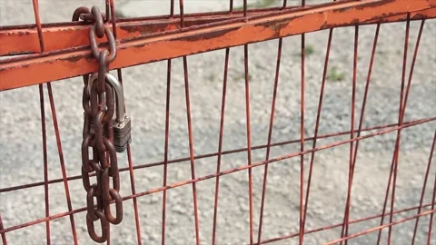 Chain and pad key lock on orange locked gate for dirt yard parking lot, close up Stock Footage 249103209
