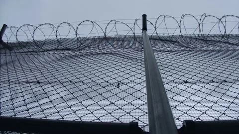A chain-link fence with barbed wire of the prison with cloudy sky backdrop Stock Footage 165052389