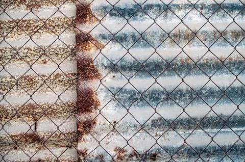 A chain link fence with extensive rust overlays corrugated metal, featuring.. Stock Photos