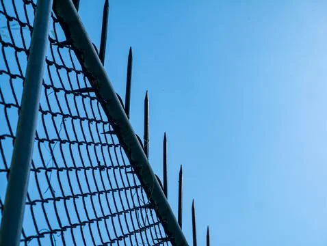 Chain Link Security Fence with Sharp Metal Spikes Against Clear Blue Sky 库存照片