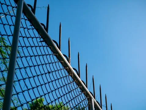 Chain Link Security Fence with Sharp Metal Spikes Against Clear Blue Sky Stockfoto's