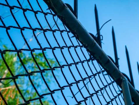 Chain Link Security Fence with Sharp Metal Spikes Against Clear Blue Sky Stock Photos