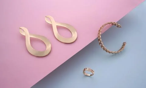 Chain shape bracelet and ring with golden modern earrings pair on pink and bl Stock Photos