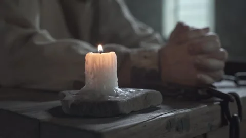Chained hands of a prisoner folded in prayer next to a candle, tracking shot 스톡 동영상 337648716