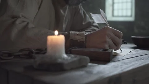 Chained hands of prisoner writing on parchment, with candle in the foreground Stock Footage 340079887