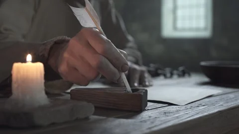 Chained hands of prisoner writing on parchment next to a candle, camera tracking Video stock 340502640