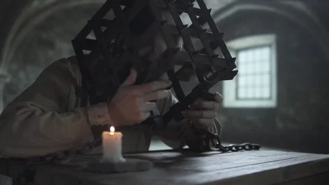 Chained inmate touching iron bars of a head cage and dropping hands onto table Stock Footage 340322874