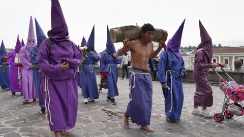 Chained man carrying log with Cucuruchos surrounding him during Jesus del Gran Stock Footage 333485124