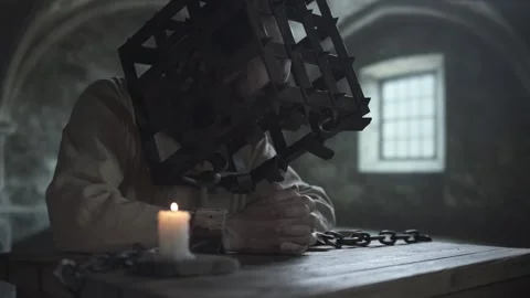 Chained prisoner with an iron cage on his head praying with clasped hands  Vídeo Stock 339631115
