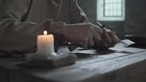 Chained prisoner sharpening a quill near a burning candle Vídeo Stock 340824386