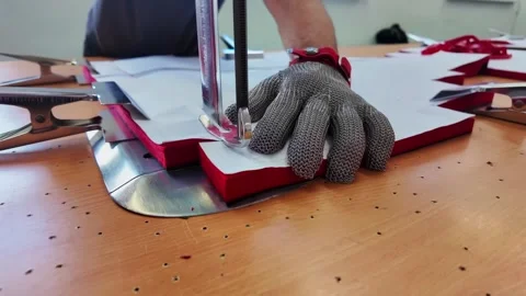 Chainmail gloved hand pressing paper pattern onto red edged material beside Stock Footage 345978637