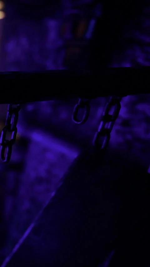 Chains hang in a dimly lit space with purple light and textured surfaces Stock Footage 331755624