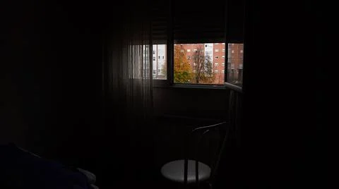 A chair stands by an open window in a dark room Stock Photos