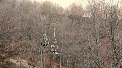 Chairlift with empty seats passing through bare autumn forest on ski resort Stock Footage 324851216