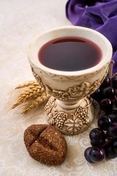Chalice with red wine, bread, grapes, and wheat on a patterned fabric Foto stock