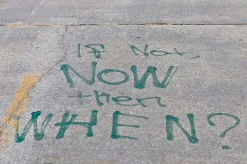 Chalk-written question 'IS NOW THEN WHEN?' on rough concrete Stock Photos