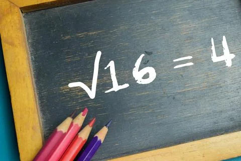 Chalkboard with phrase ?16 = 4 square root equation on wooden desk. Stock Photos