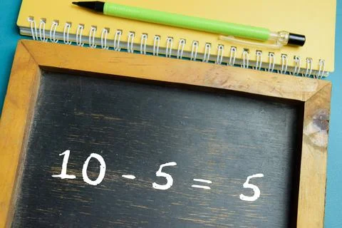 Chalkboard with phrase simple 10-5=5 math equation on wooden desk. Stock Photos