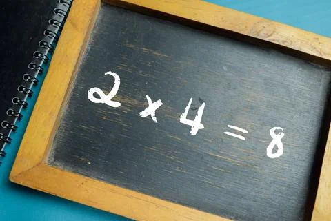Chalkboard with phrase simple 2x4=8 math equation on wooden desk. Stock Photos