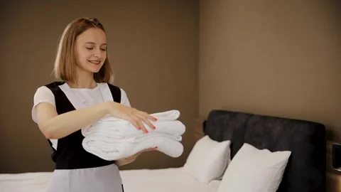 Chambermaid holding a stack of clean, folded white towels in hotel bedroom Stock Footage 324721786