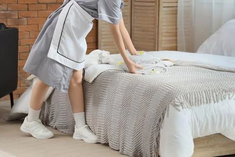Chambermaid putting stack of clean towels with plumeria flowers on bed in hot Stock Photos