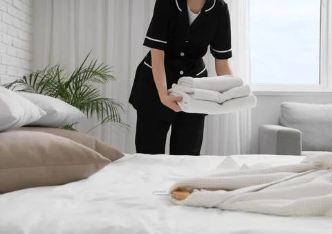 Chambermaid putting stack of clean towels on bed in hotel room Stock Photos