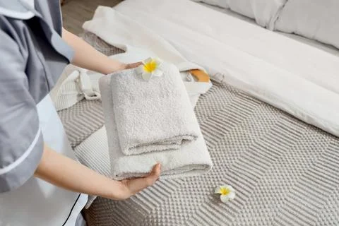 Chambermaid putting stack of clean towels with plumeria flowers on bed in hot Stock Photos
