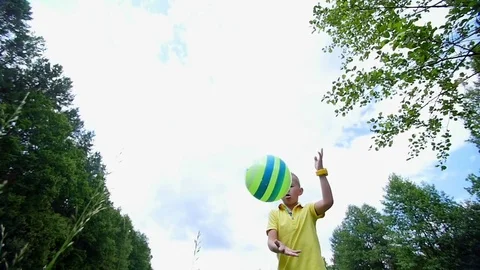 On a chamomile meadow, near a forest, a boy, a child, plays ball, throws it Stock Footage
