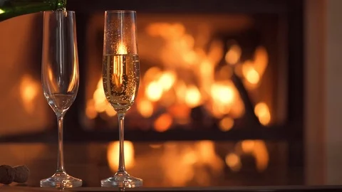 Champagne in two glasses on table in front of burning fireplace. 動画素材 79874352