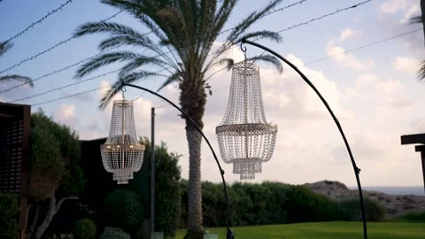 Chandeliers hang by palm trees with a view of the sky and ocean at sunset Stock Footage 347325282