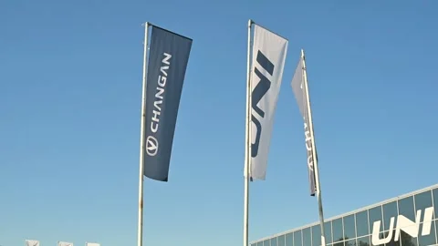 Chang'an flags wave in the wind outside a car dealership under clear skies. 库存影片 344672717