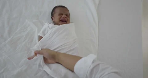 Change diaper swaddling a crying black African newborn baby on a bed Stock Footage 338361087