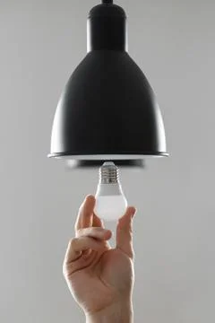 Changing the bulb for led bulb in floor lamp in black colour. On light gray b Stock Photos