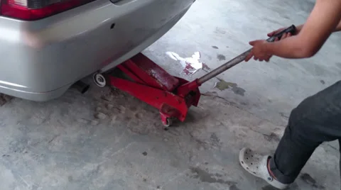 Changing tyre: Man lifting car up using floor jack Stock Footage 39213631