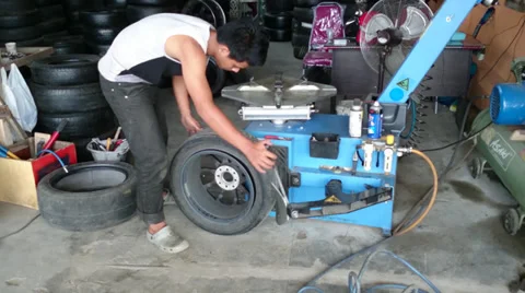 Changing tyre: Man removing a worn off tyre from a wheel rim in a garage Stock Footage 39192910