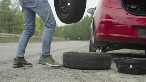 Changing a wheel in a red car. A man in a vest takes a spare tire Stock Footage 221243194