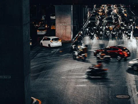 Chaotic Nighttime Traffic Intersection with Motorcycles and Cars Under Overpa 库存照片