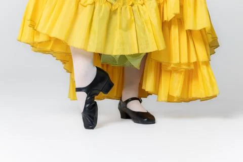 Character dancer feet in black dance shoes and yellow skirt close up on whi.. Stock Photos
