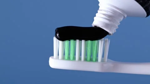 Charcoal toothpaste on toothbrush over blue background. Stock Footage 276156042