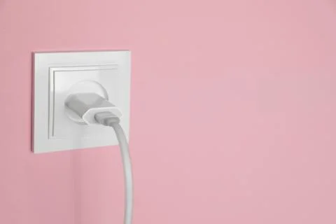 Charger adapter plugged into power socket on pink wall, space for text. Elect Stock Photos